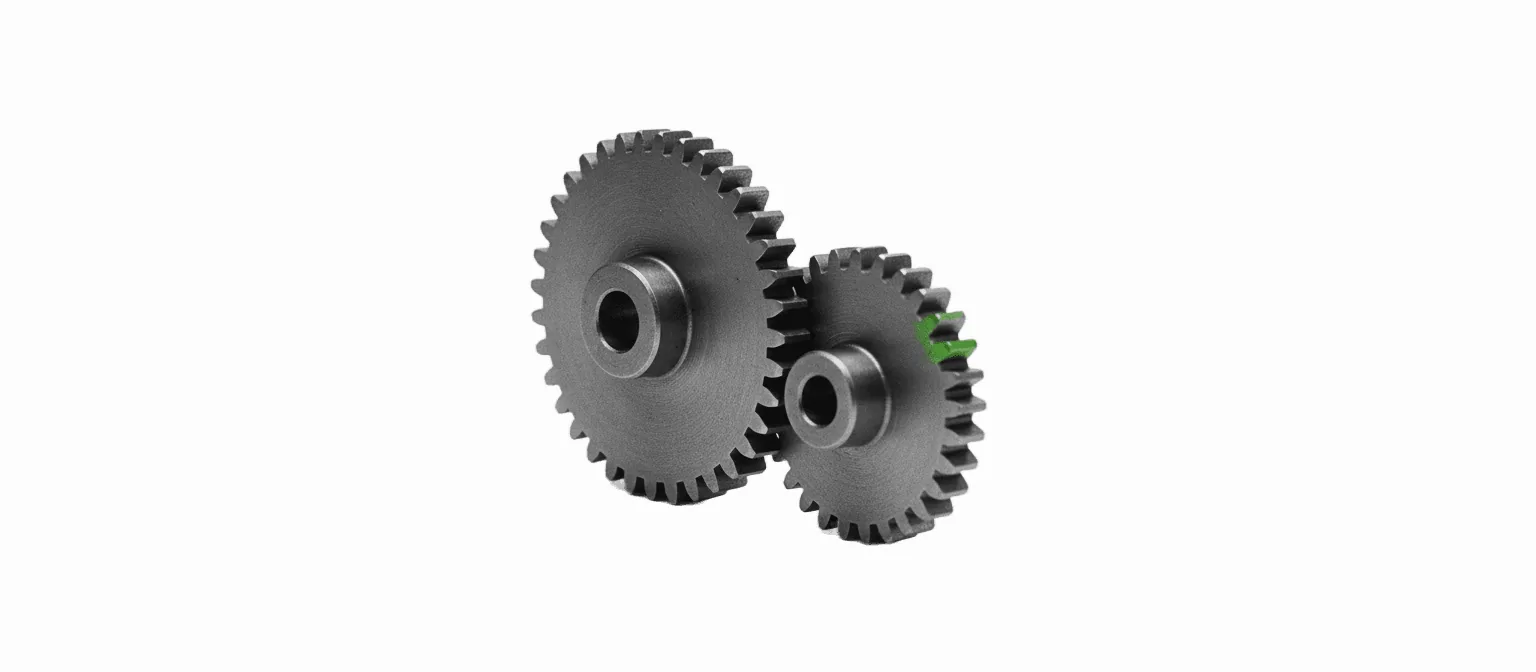 Two interlocking brass gears meshed together with one tooth picked out in vivid green, on a white background