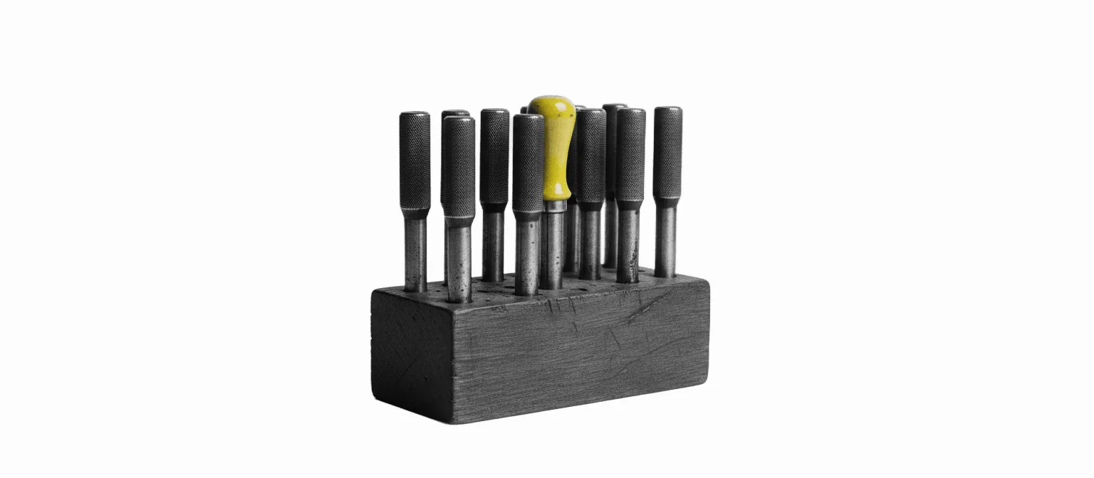A set of silversmith's steel stamps standing in a wooden bench holder, one with a vivid yellow handle standing taller than the rest