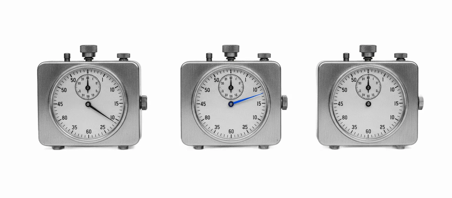 Three vintage mechanical interval timers in a row, the middle one running with a vivid blue sweep hand, black and white.
