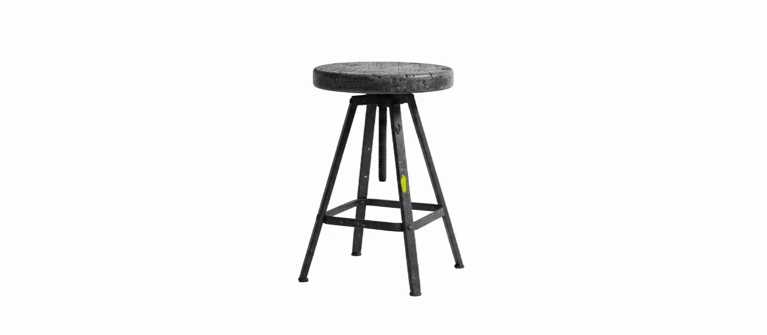 A worn wooden machinist's shop stool with steel legs and an adjustable screw post, a small yellow paint fleck on the brace, black and white.