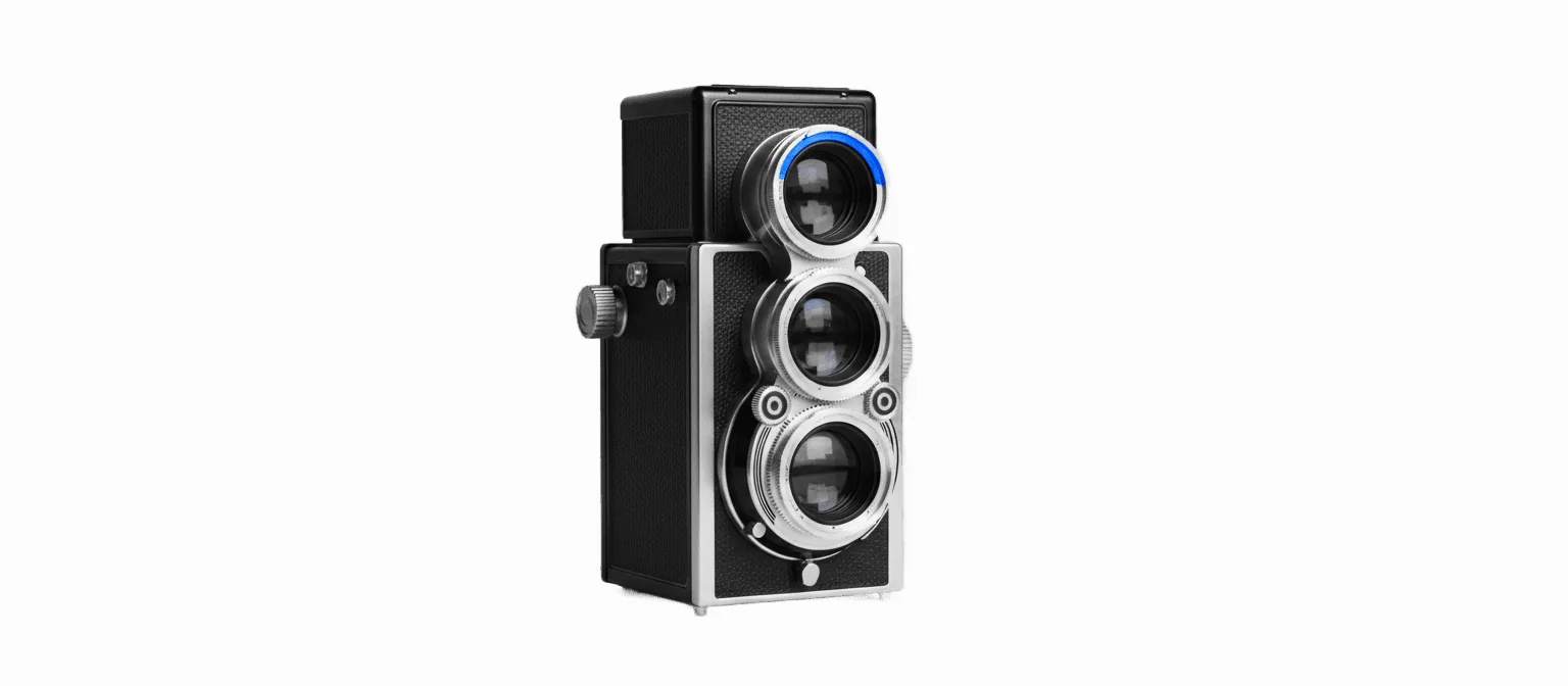 Black-and-white photograph of a vintage 1960s twin-lens reflex camera at a three-quarter front angle on a white background, with a vivid blue filter ring on one of the two lenses