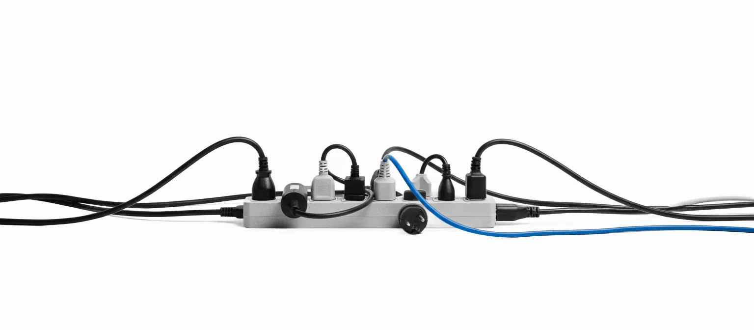 A power strip completely full of plugged-in extension cords, one cord in vivid blue among the monochrome — every connection deliberate