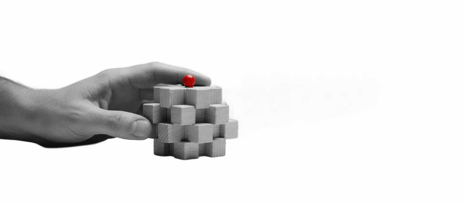 Black-and-white photo of a craftsman's hand on one finished piece with an identical row receding behind it — human craft multiplied by machine, one red detail on the original
