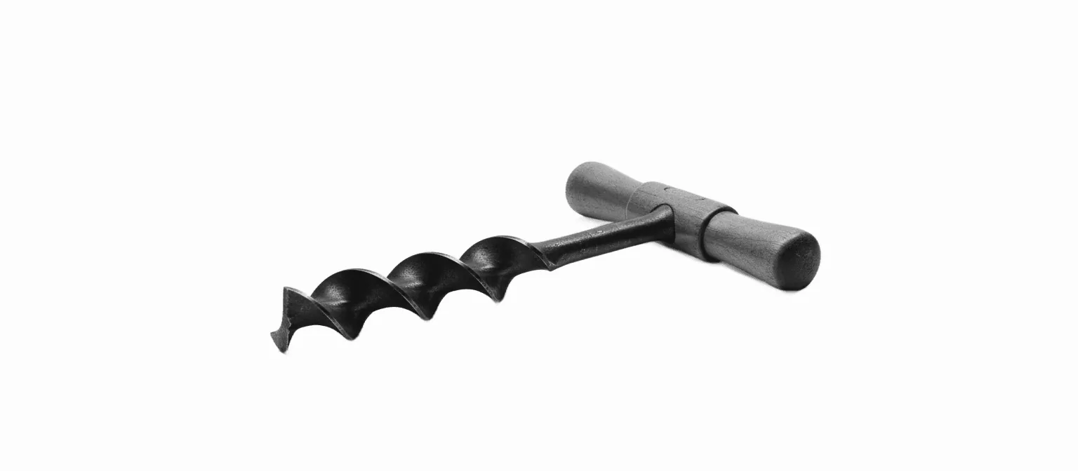 A vintage T-handle wood-boring auger with a long helical shaft, resting after work — manual labor as the substrate beneath the machine
